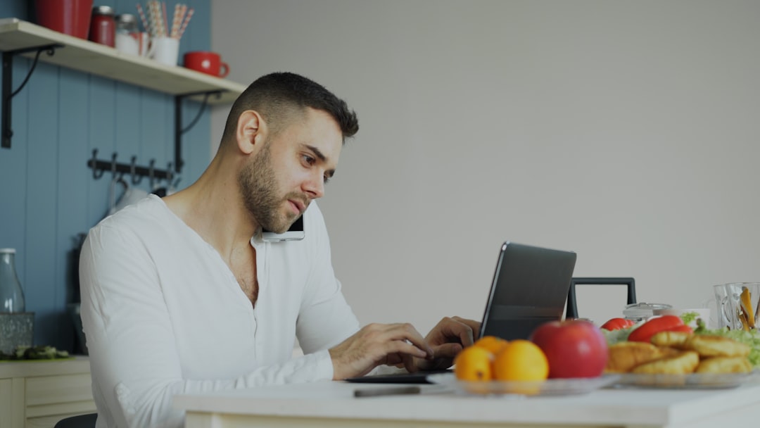 Man on phone and laptop at kitchen table - Photo by Vitaly Gariev on Unsplash