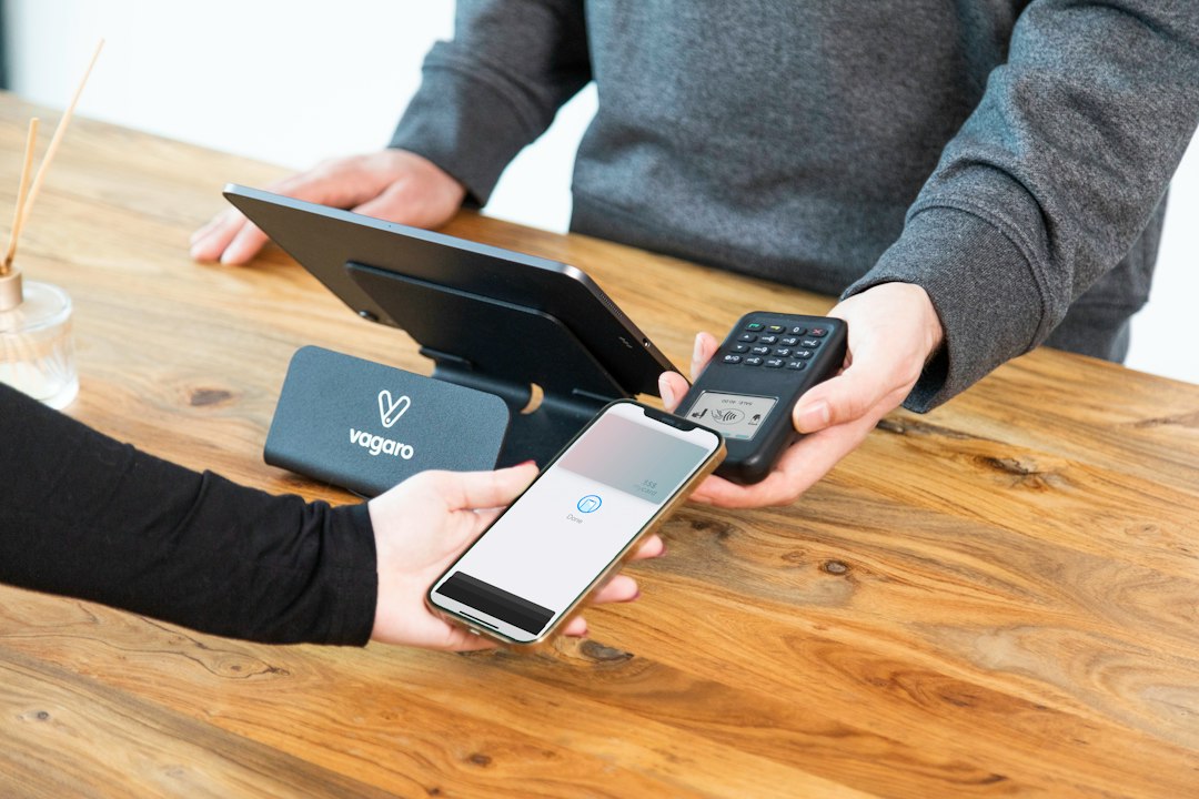 a person holding a cell phone and a laptop on a table - Photo by Vagaro on Unsplash