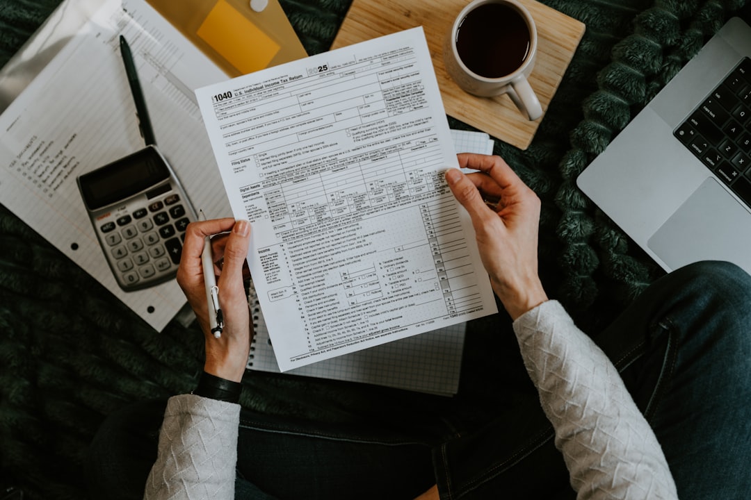 Hands holding tax forms with calculator and laptop. - Photo by Kelly Sikkema on Unsplash