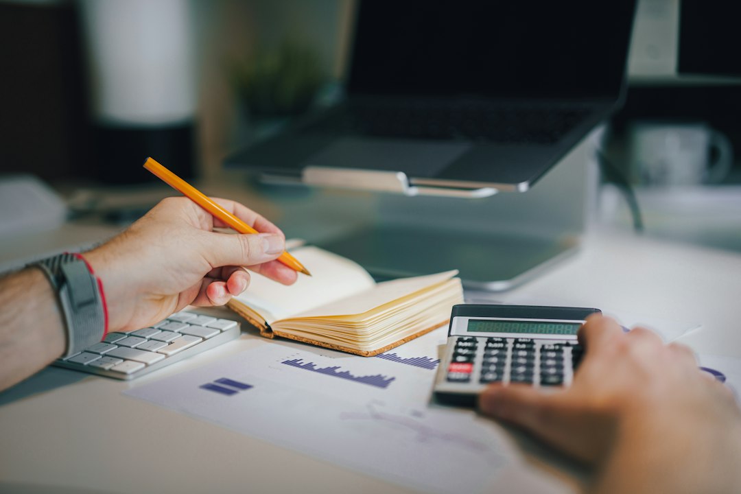 a person sitting at a desk with a calculator and a notebook - Photo by Jakub Żerdzicki on Unsplash