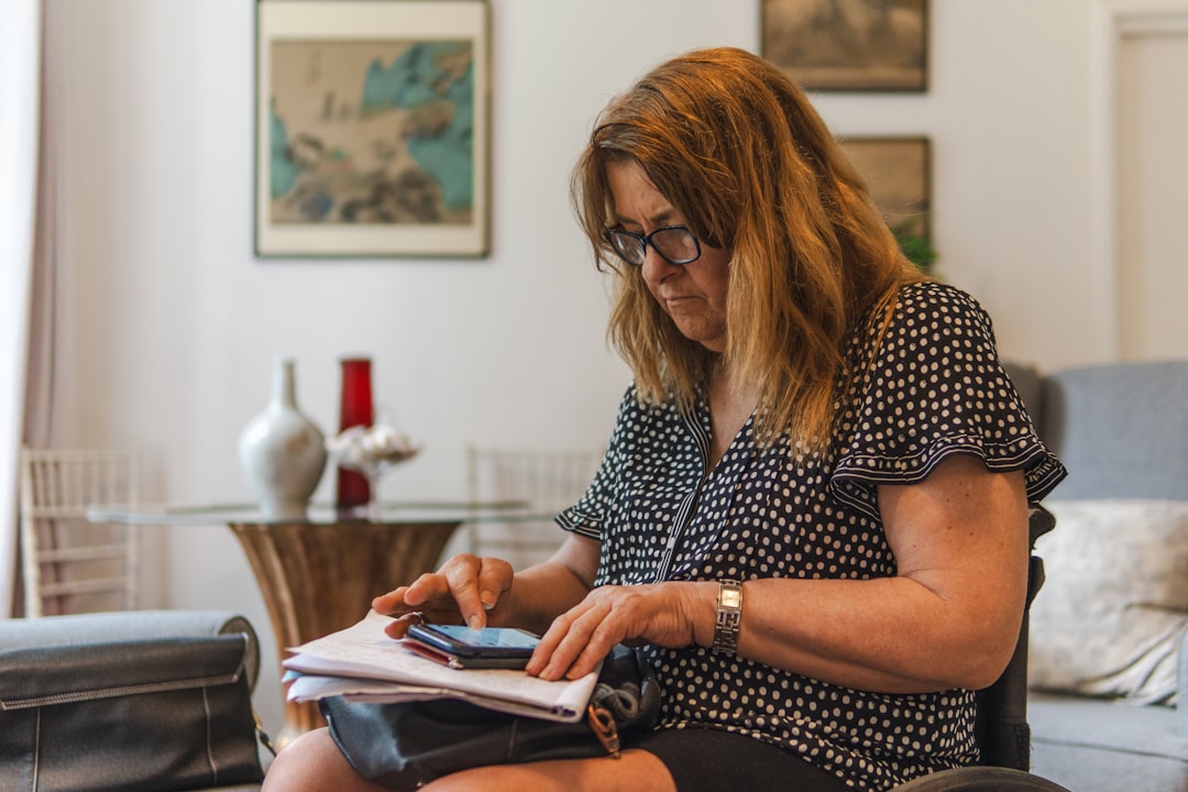 Woman looking at phone while writing on paper — Photo by Centre for Ageing Better on Unsplash