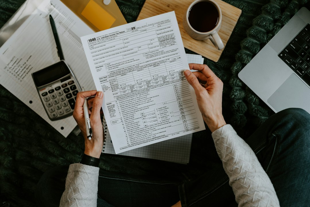 Hands holding tax forms with calculator and laptop - Photo by Kelly Sikkema on Unsplash
